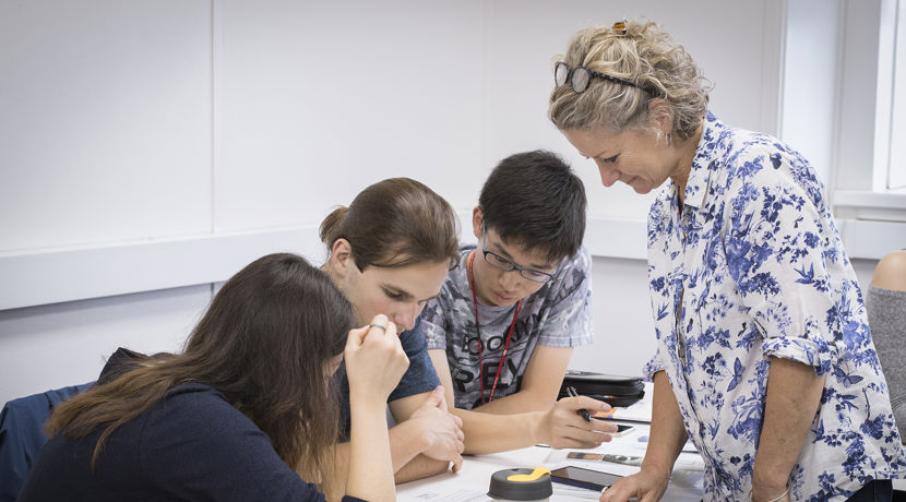 Teacher helping three students sitting at a desk with their work.