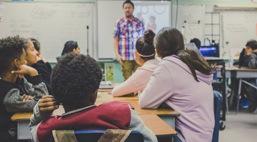 Classroom of young students looking towards their teacher. Several white boards are in the background.