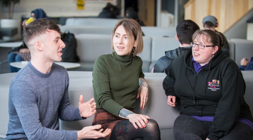 Three students having a conversation while sitting on a sofa at one of the college's communal areas.