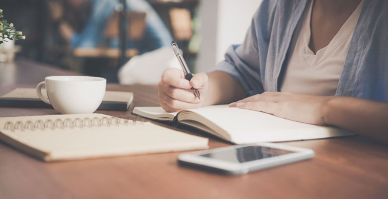 Student writing in a notebook in a café with a cup of coffee.