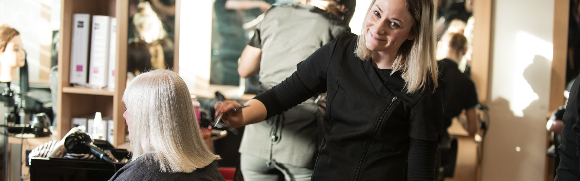 Hairdressing student combing a clients blonde hair in the salon.