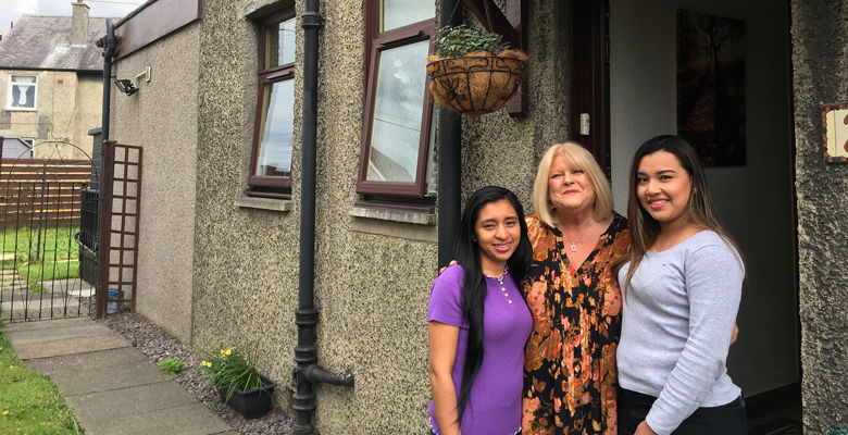 Two exchange students standing with their host outside a house.