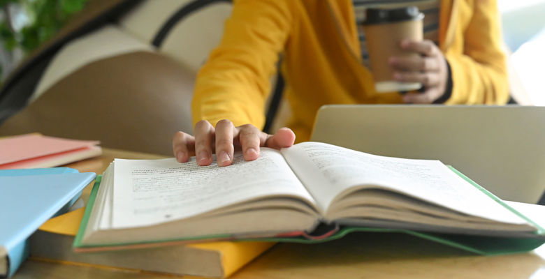 Person holding a coffee cup is holding open a page on a book.