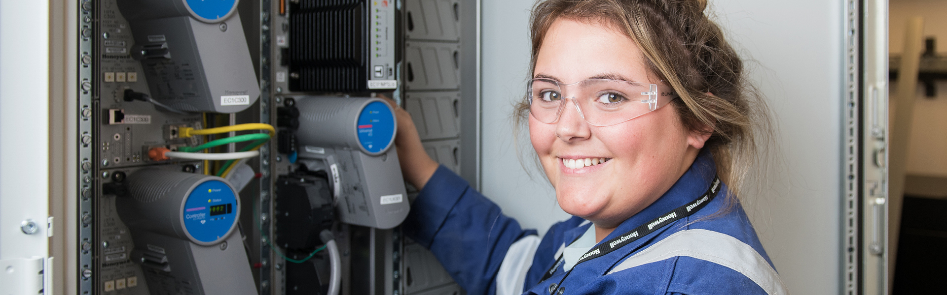 Oil and gas student smiling as they work with cables, wearing blue overalls and safety goggles.