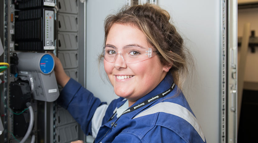 Oil and gas student smiling as they work with cables, wearing blue overalls and safety goggles.