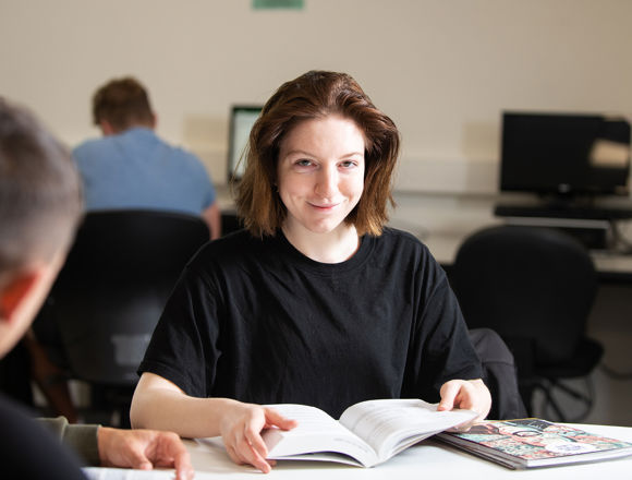 Smiling student reading a book in the library.