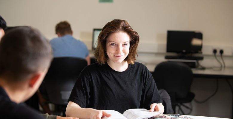 Smiling student reading a book in the library.