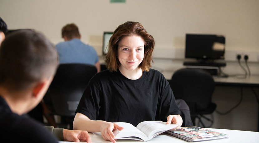 Smiling student reading a book in the library.