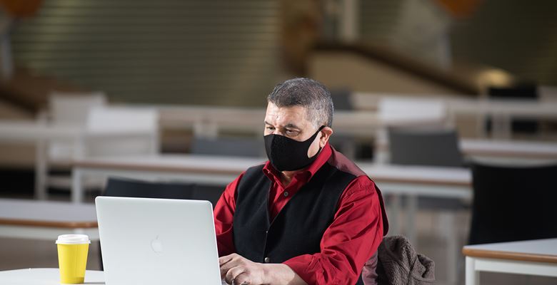Student working at a laptop in college wearing a face covering.