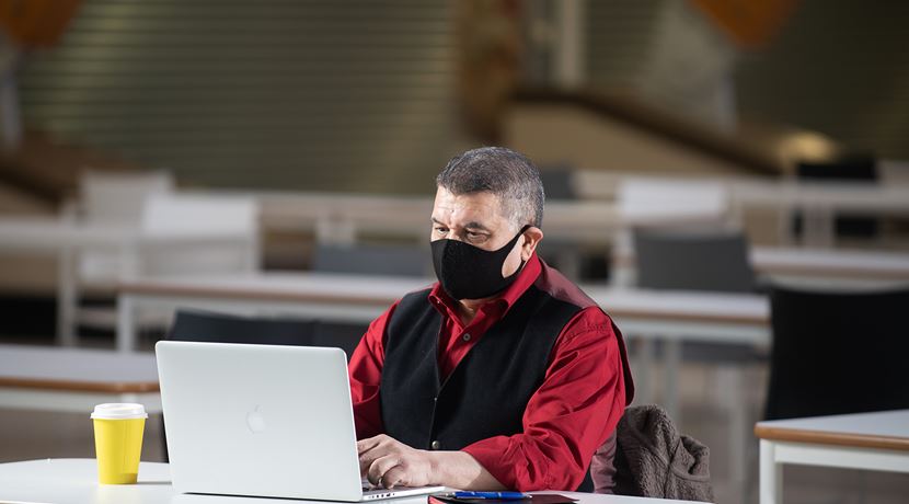 Student working at a laptop in college wearing a face covering.