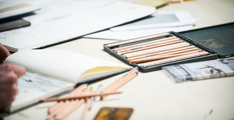 Sketchbooks and pencils are scattered over a desk. 