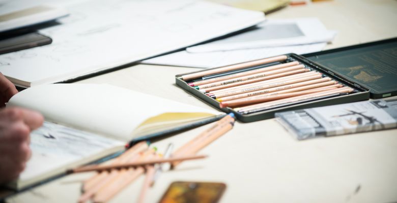 Sketchbooks and pencils are scattered over a desk.