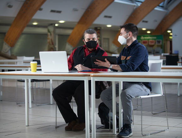 Two students wearing face coverings, working on laptops in a communal area at Granton campus.