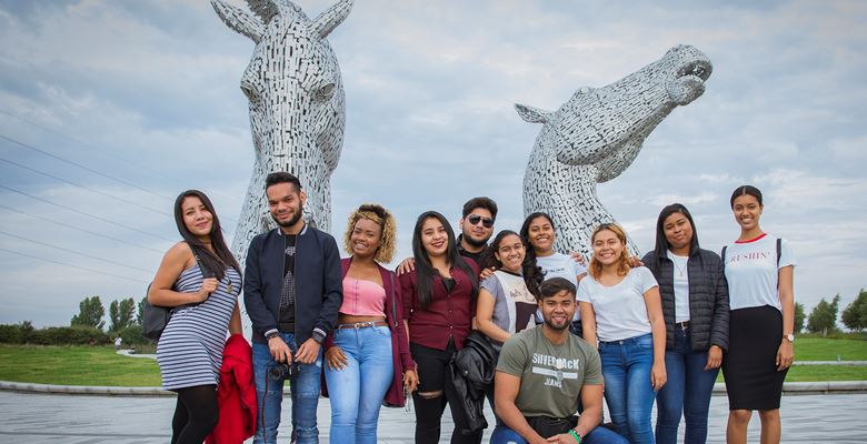Group of students on a social programme standing for a group photo at the Kelpies, which are a large metal horse structure.