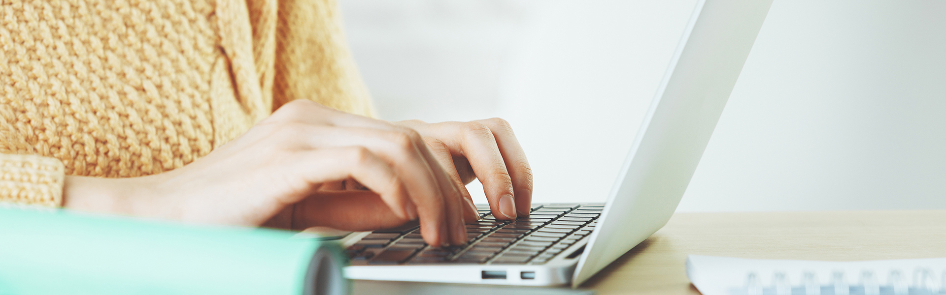 Person typing on a laptop with books on the desk.