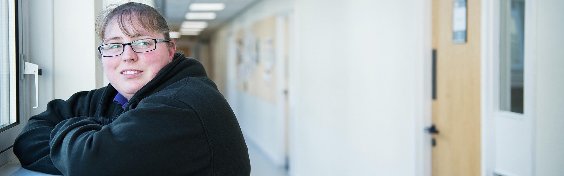 Smiling student leaning on a windowsill in a corridor.
