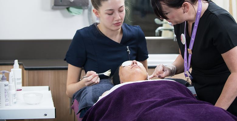 Beauty student giving a client a facial in the salon while a lecturer observes. 