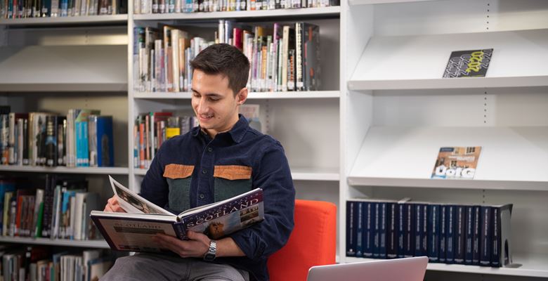 Young male student reading a book in the library. 