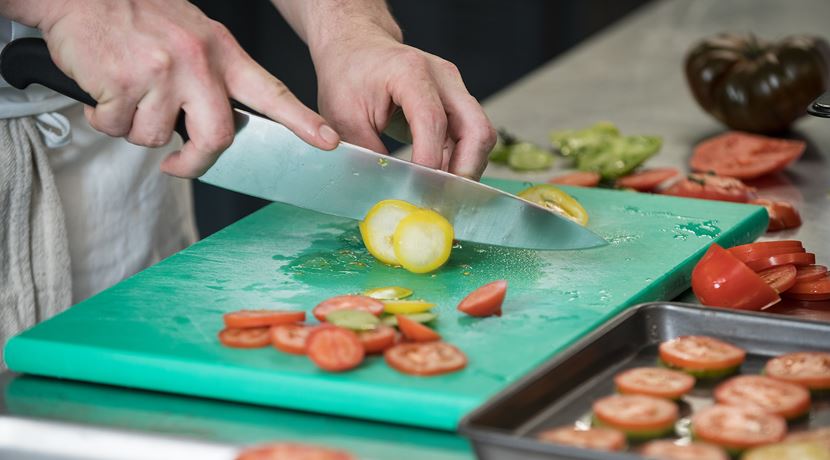 Close up of cookery student chopping vegetables in a training kitchen. 