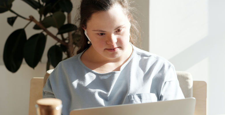 Student with earphones looking at their laptop with a large plant situated behind them.