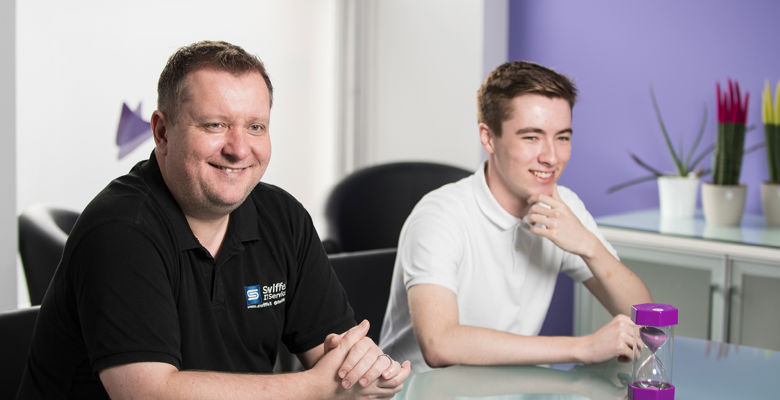 Young student working at a desk in an open plan office during a work placement next to their mentor.