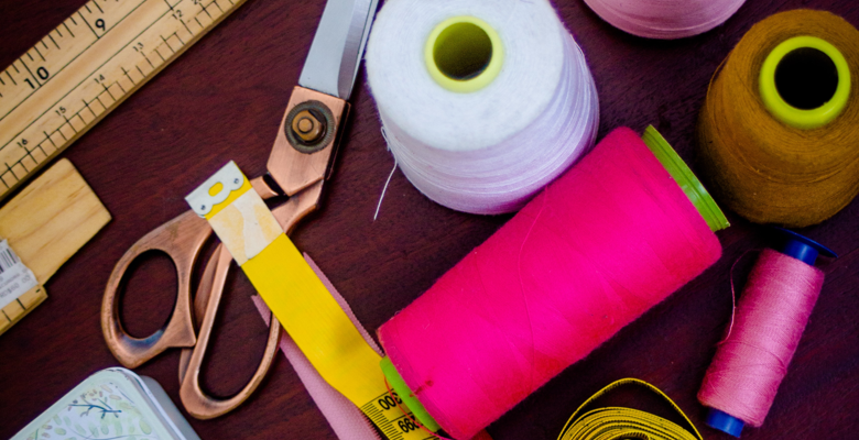 Sewing equipment on a desk. The equipment includes threads, scissors, beads and tape measures.