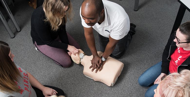 Health students learning CPR on a dummy in a classroom.