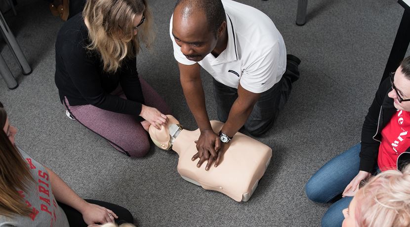 Health students learning CPR on a dummy in a classroom.