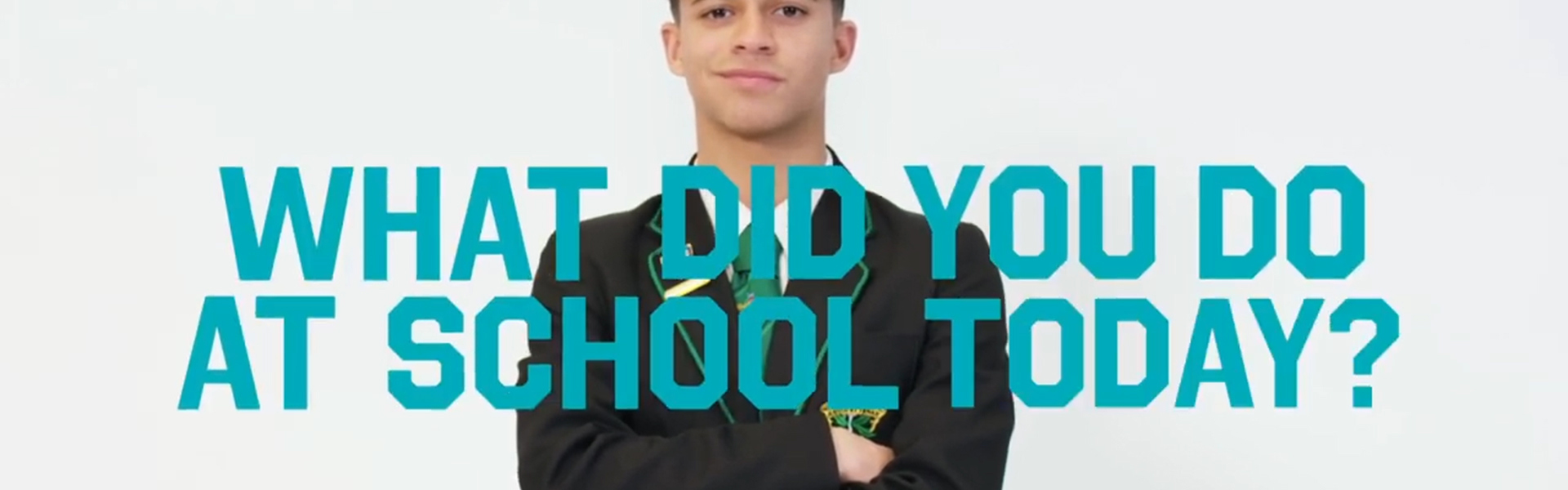 School pupil wearing a blazer has their arms crossed and is smiling. Text reads "What did you do at school today?"