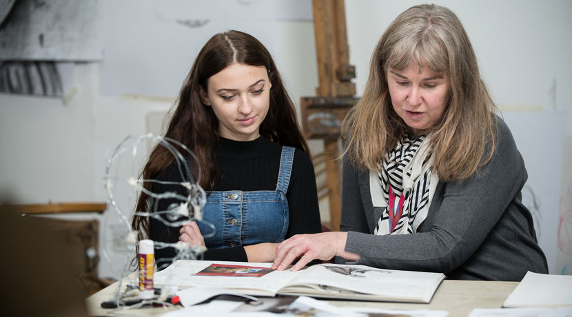 Lecturer helping a young student with their work in an art classroom.