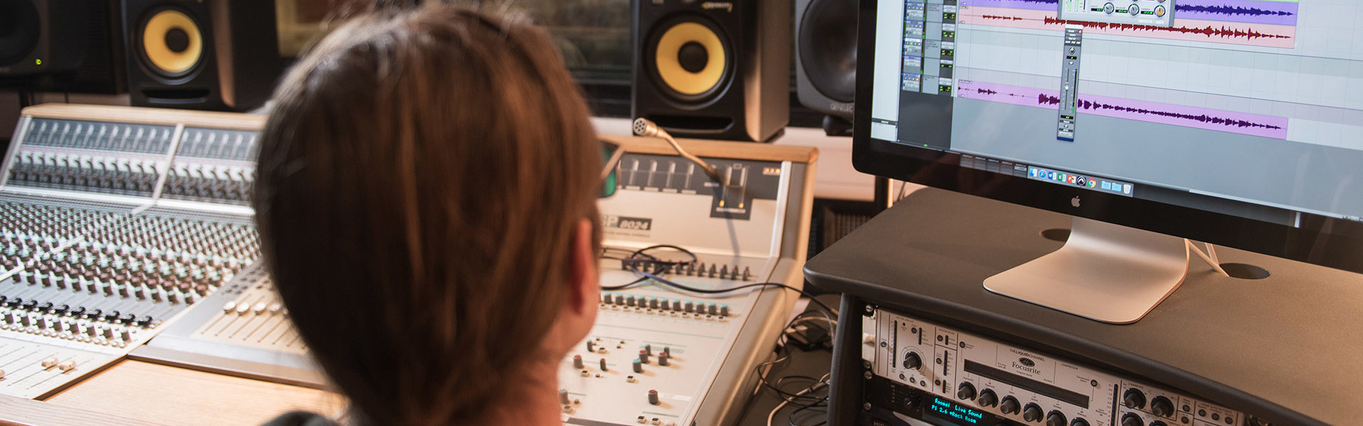 Student is working in a recording studio and looking at a computer screen with their work on it.