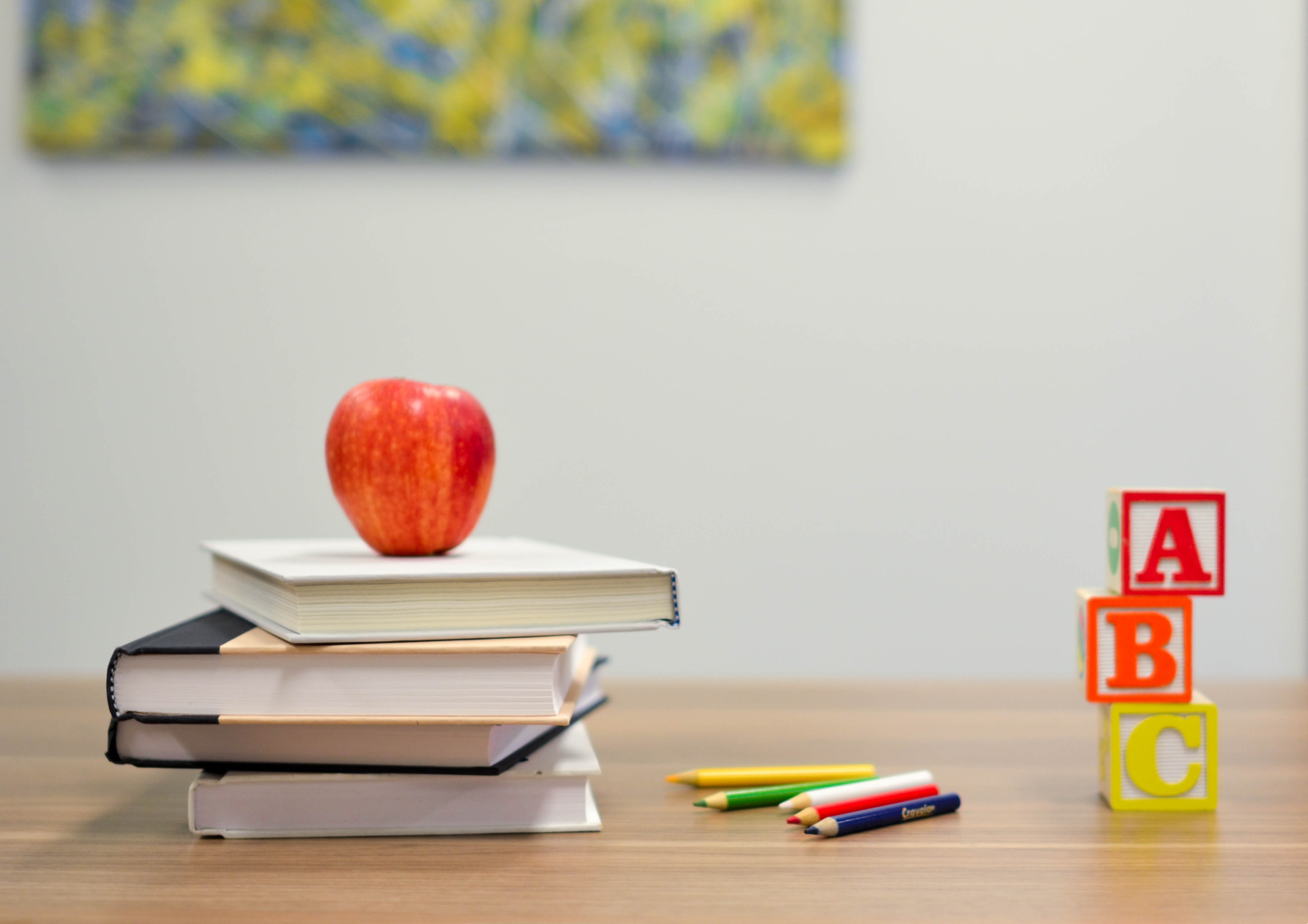 Books, pencils and building blocks sit on a teacher's desk, with an apple on top of the books.