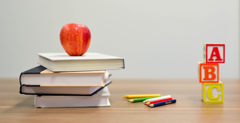 Books, pencils and building blocks sit on a teacher's desk, with an apple on top of the books.