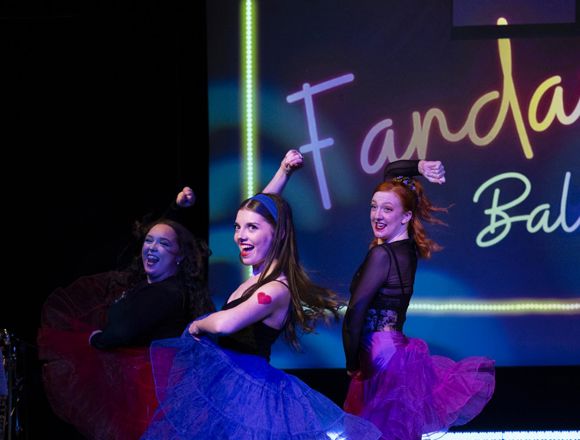 Three dancers perform on stage in colorful tutus, showcasing dynamic movement with a bright background that reads “Fandango Ballet.”