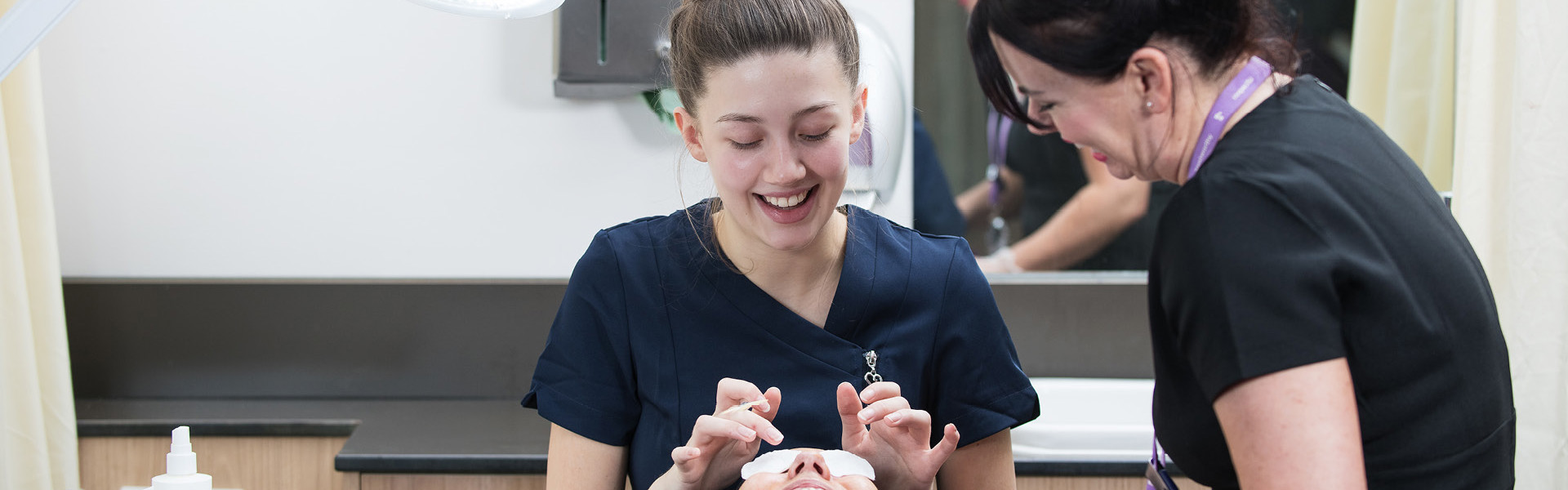 Beauty student giving a client a facial in the salon while a lecturer observes.