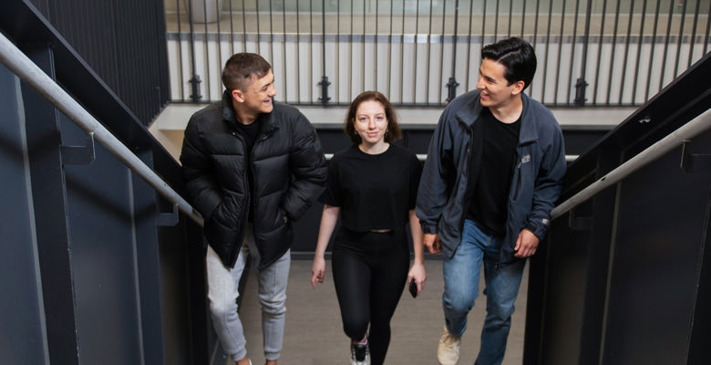 Three students talking and laughing with each other while walking up stairs at a college building.