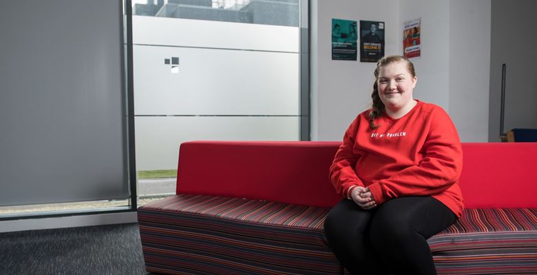 Emily sitting on a red sofa at college. 