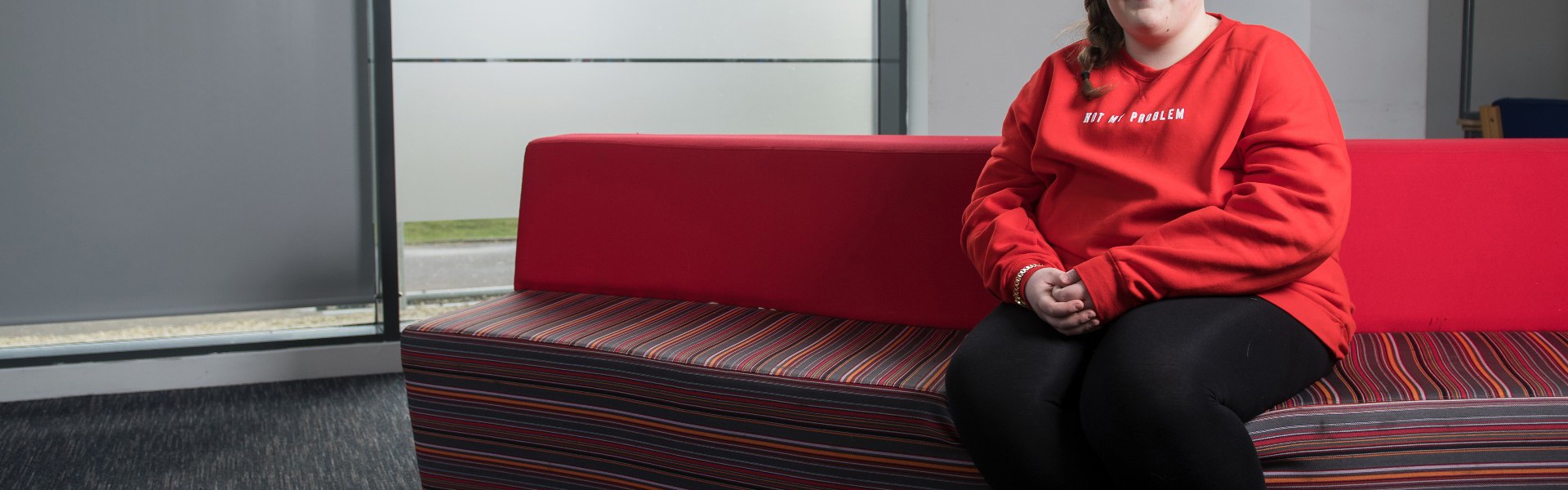 Emily sitting on a red sofa at college.