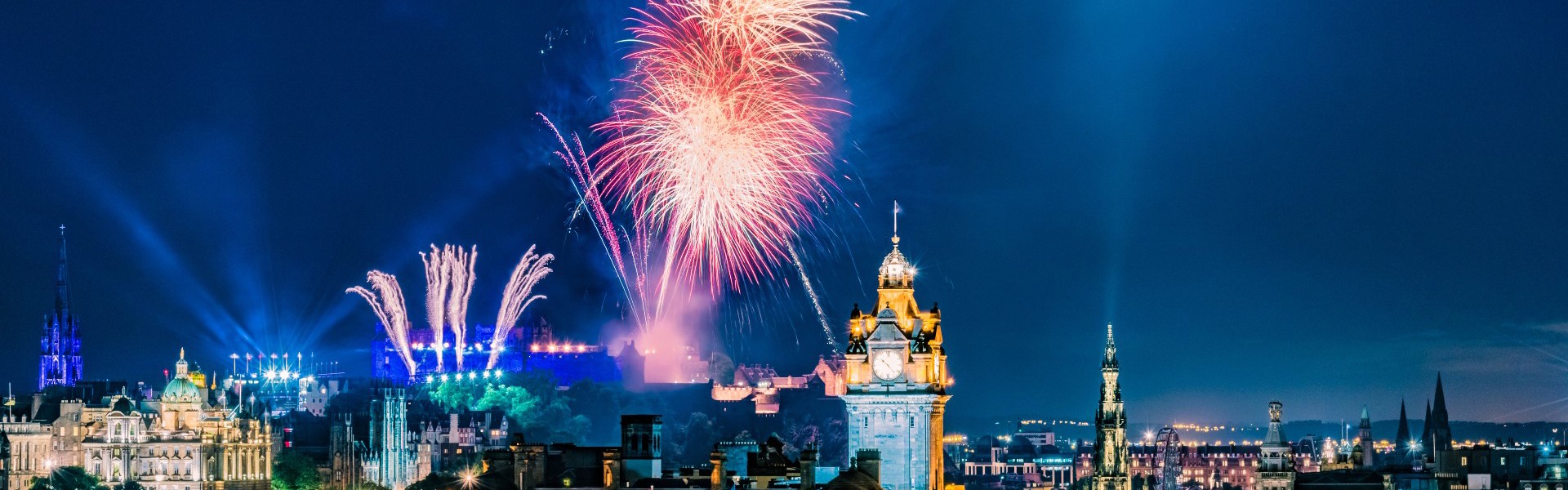 Bright fireworks against a dark blue sky and Edinburgh's skyline.