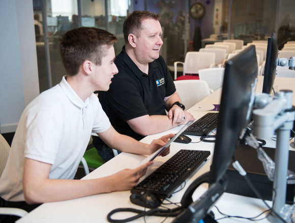 Young student working at a desk in an open plan office during a work placement next to their mentor.