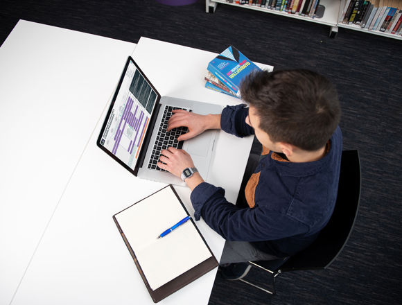 Student at a desk in the library with their laptop open, looking at Edinburgh College progression maps on the screen.