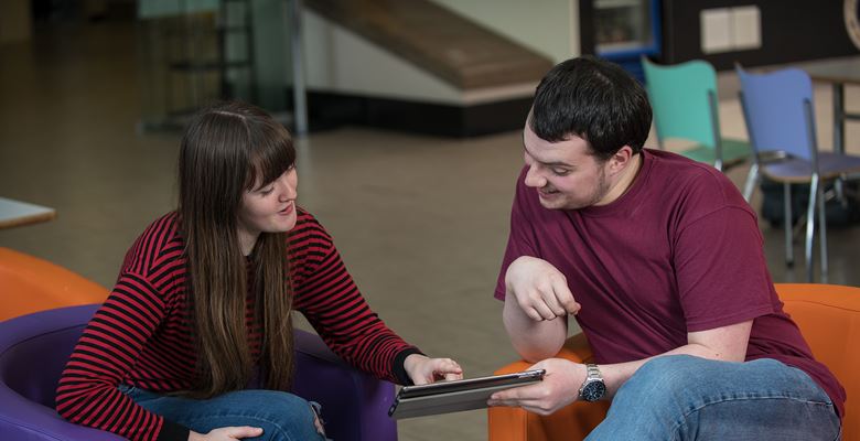 Two students talking about something while looking at something on their tablet screen.
