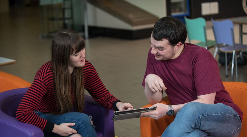 Two students talking about something while looking at something on their tablet screen.