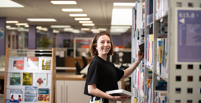 Student picking out a book from a library shelf.