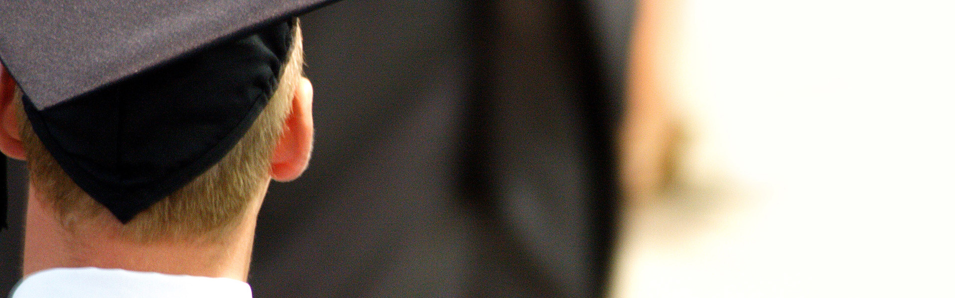 Back on a persons head who is wearing a black graduation cap and gown.