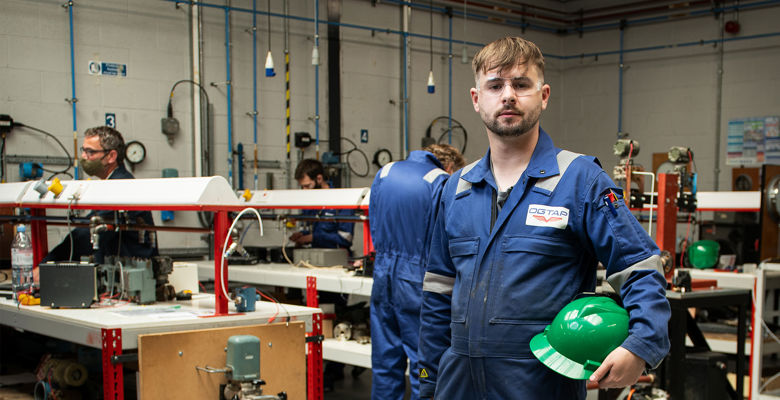 Oil and gas student smiling in an engineering classroom, holding their hard hat.
