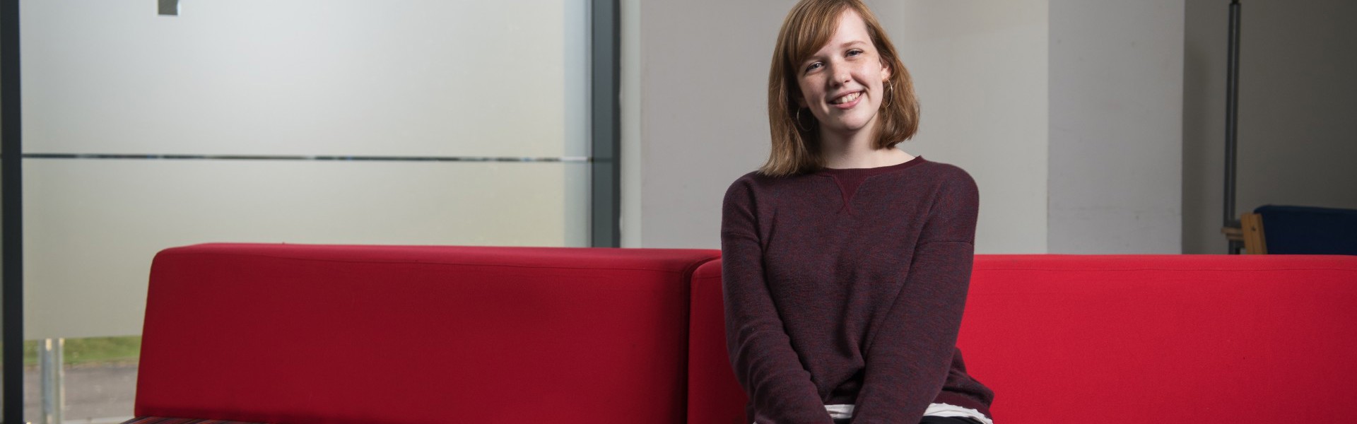 Kate Baird sitting on a red sofa at college.