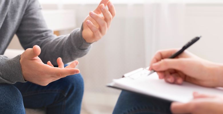 Close up of two people speaking during a counselling session. One person is taking notes on a notepad. 