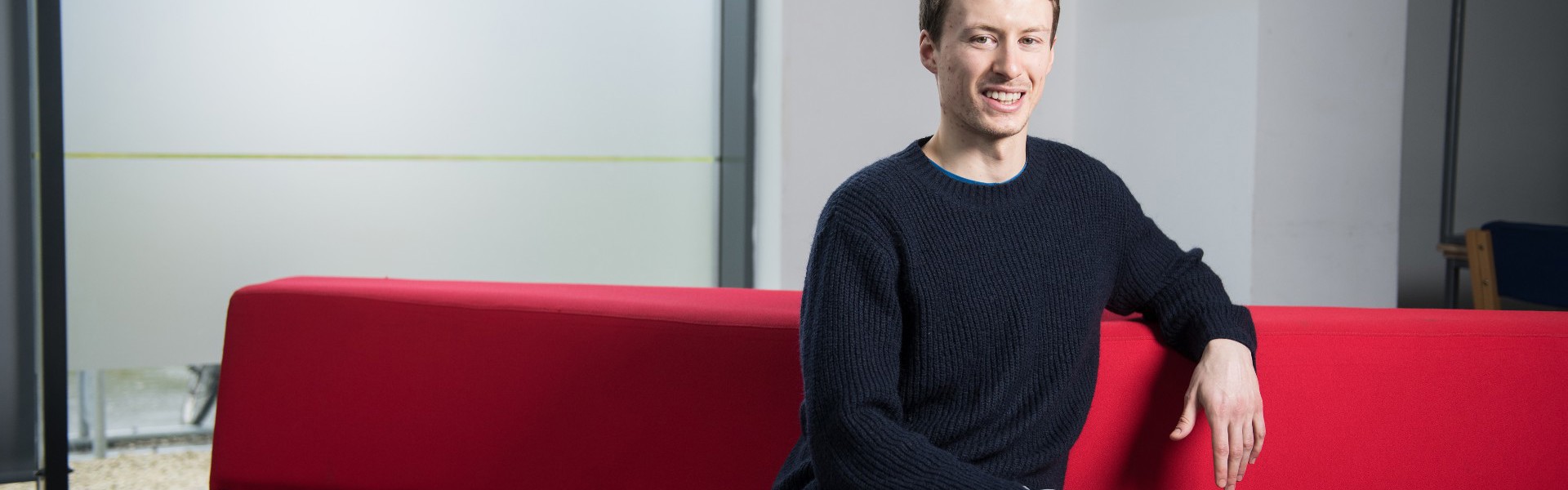 Peter sitting on a red sofa at college.