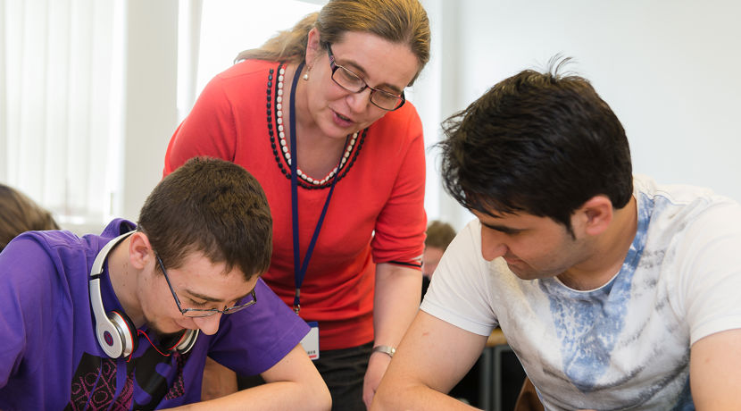 Lecturer supporting two students who are working in a classroom.